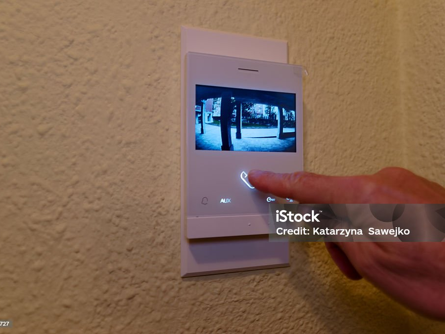Finger drückt den Türöffner an einer Innenstation mit Kamerabild