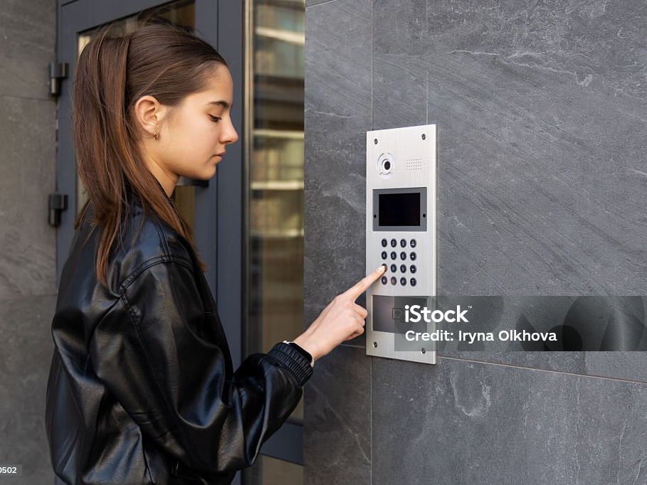 Frau tippt einen Code in die Türstation eines Wohnhauses